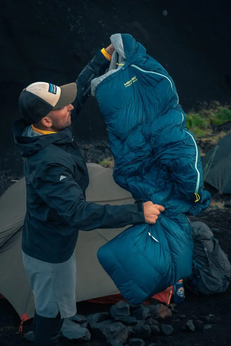 Mann, der einen blauen Schlafsack vor einem Zelt einpackt
