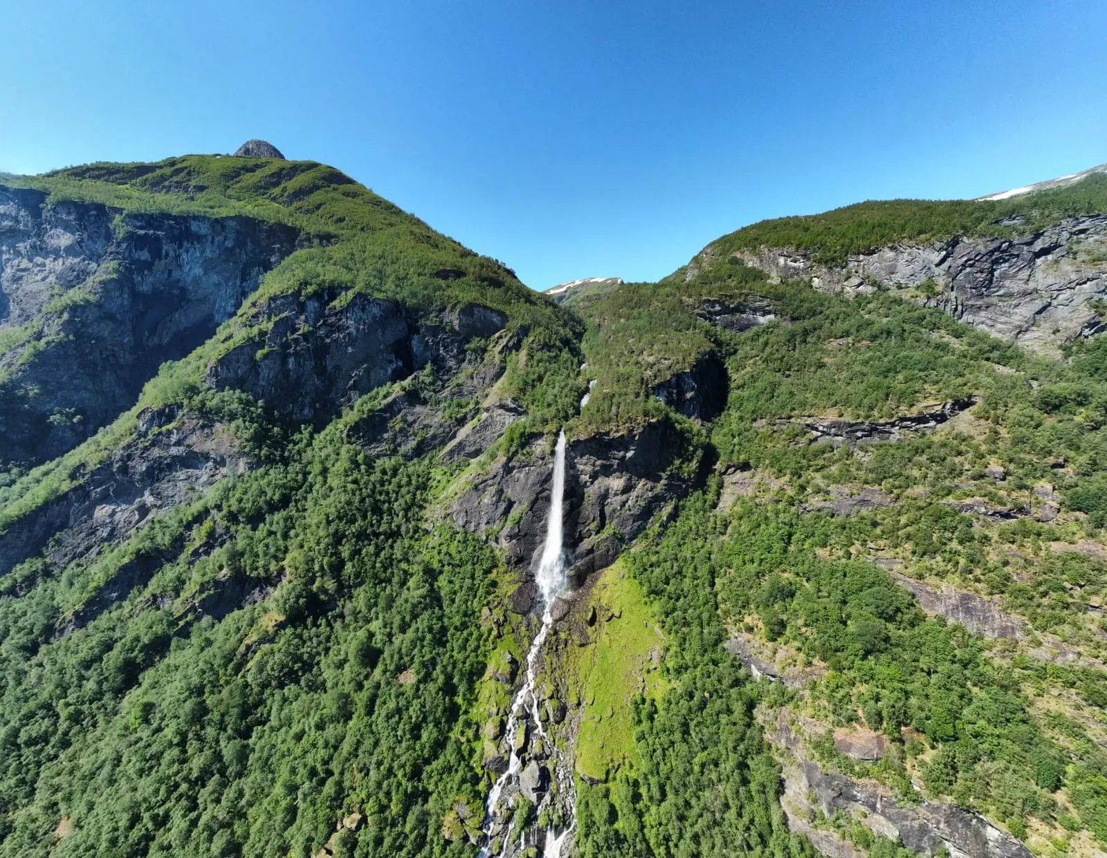 Drohnenaufnahme eines hohen Wasserfalls, der einen üppig grünen Berg hinabstürzt