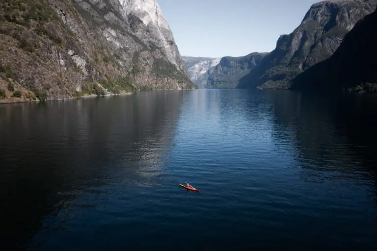 Kajakfahrer paddelt in einem roten Kajak auf einem tiefblauen Fjord