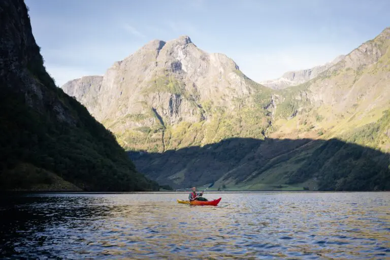 person kayaking on a fjord surrounded by mountains
