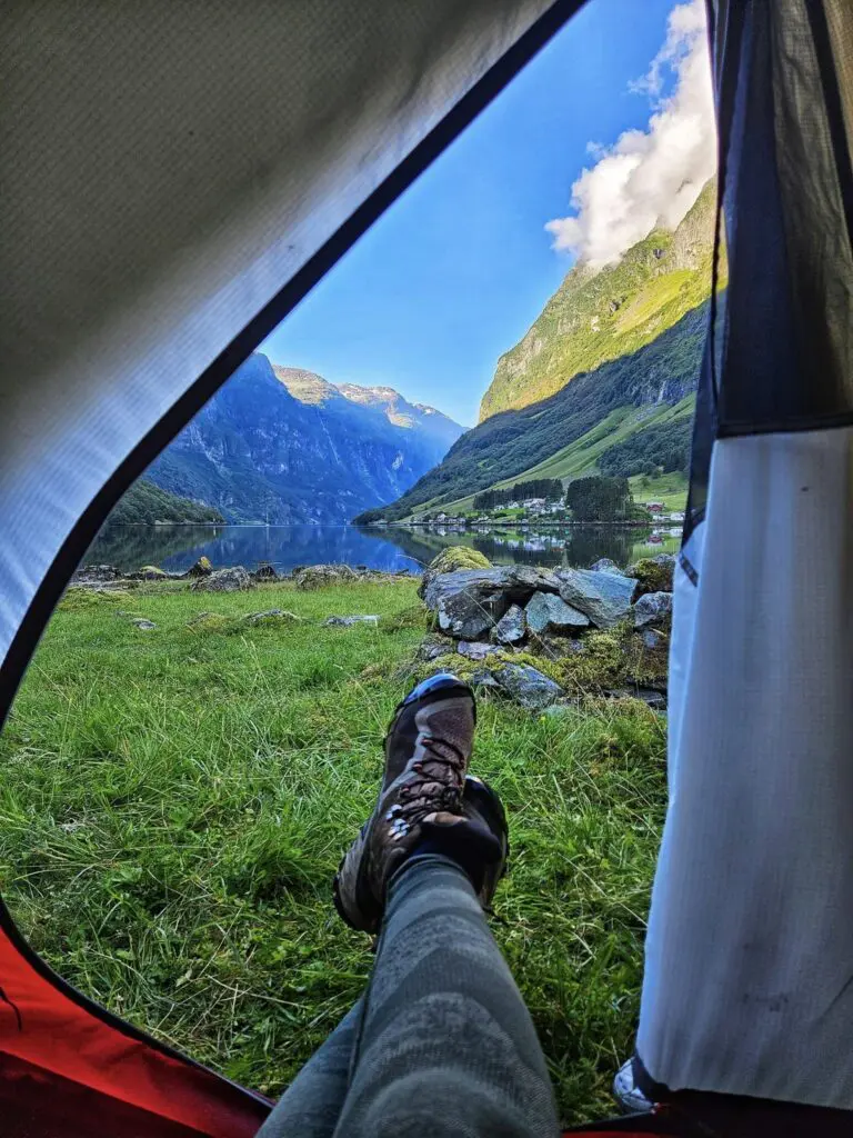 person's legs and boots inside tent overlooking a fjord