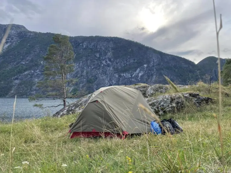 Zelt an einem See mit Bergen unter bewölktem Himmel
