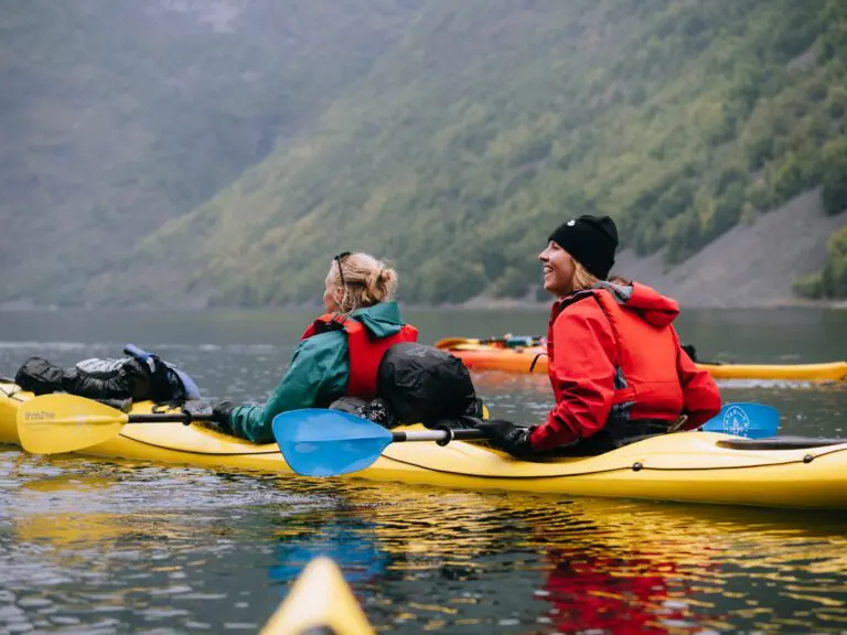 two women kayaking on a lake with mountains