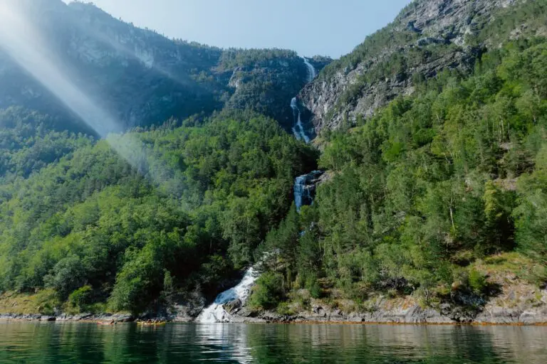 Kajakfahrer auf einem Fjord mit einem Wasserfall und Sonnenstrahlen