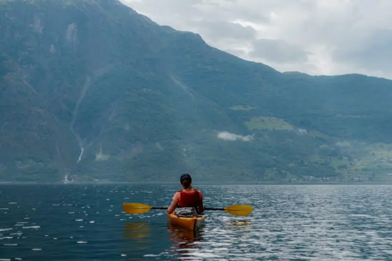 Person beim Kajakfahren auf einem ruhigen See vor einer Bergkulisse