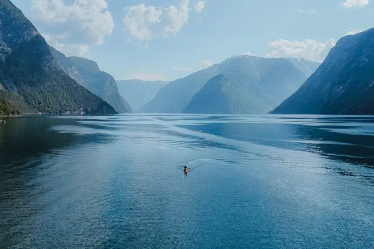 Kajakfahrer beim Paddeln in einem weiten, von Bergen umgebenen Fjord