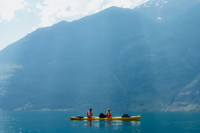 zwei Menschen beim Kajakfahren auf einem ruhigen See mit Bergen