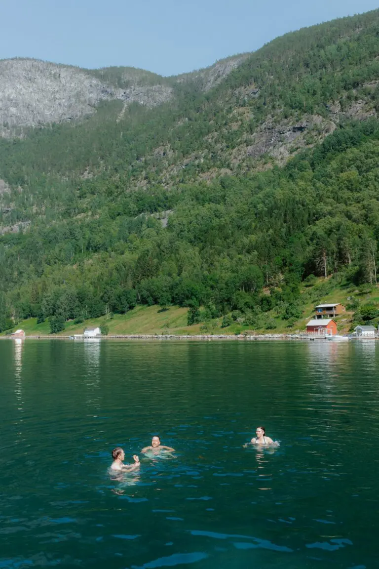 drei Frauen schwimmen in einem grünen Fjord mit Bergen