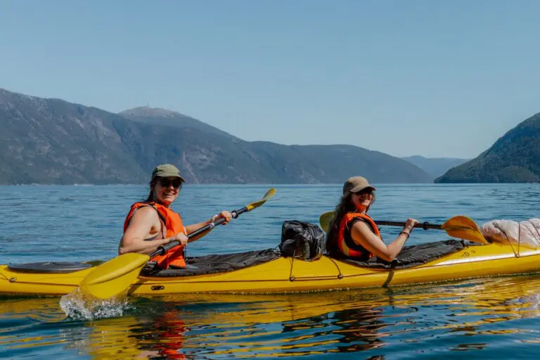 zwei Frauen beim Kajakfahren auf einem See mit Bergen im Hintergrund