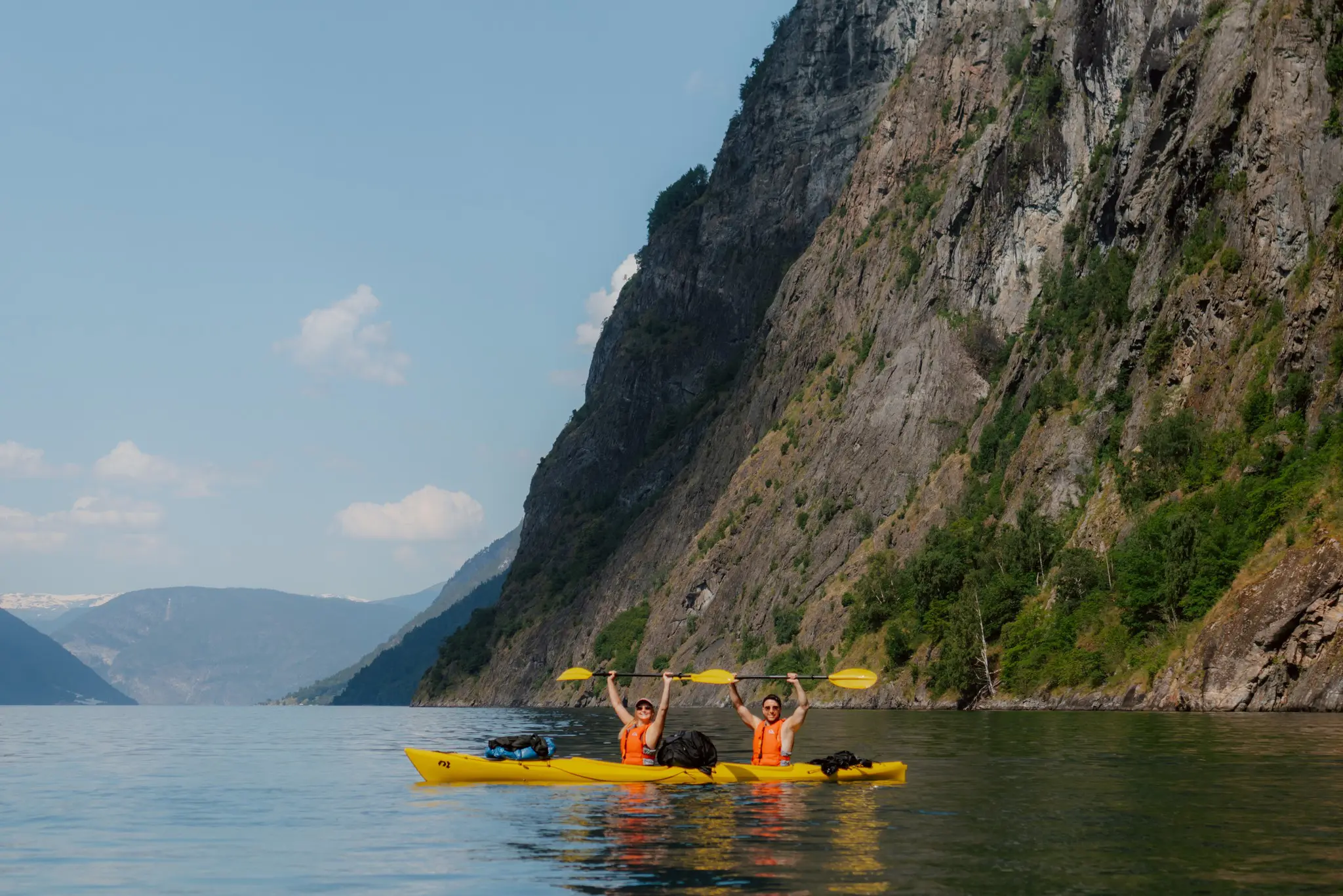 zwei Personen, die in einem Fjord Kajak fahren und ihre Paddel zum Feiern in die Höhe halten