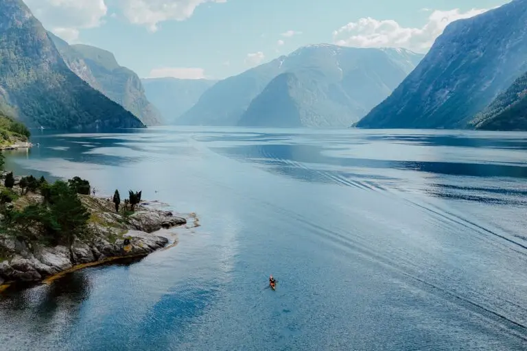 Kajakfahrer, der auf einem weitläufigen, von Bergen umgebenen Fjord paddelt