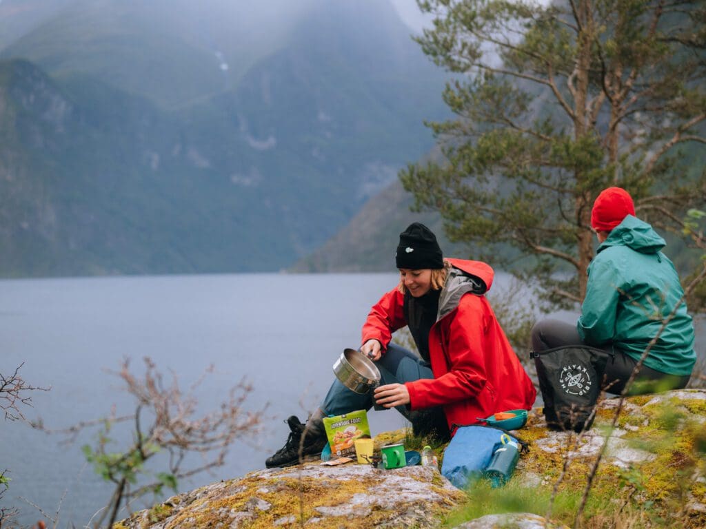 Frau kocht Wasser für Kaffee und ein Essenspaket - Kajakfahren - Norwegenfjord - Wandern in Norwegen - Kayaking - ab Flughafen Brüssel
